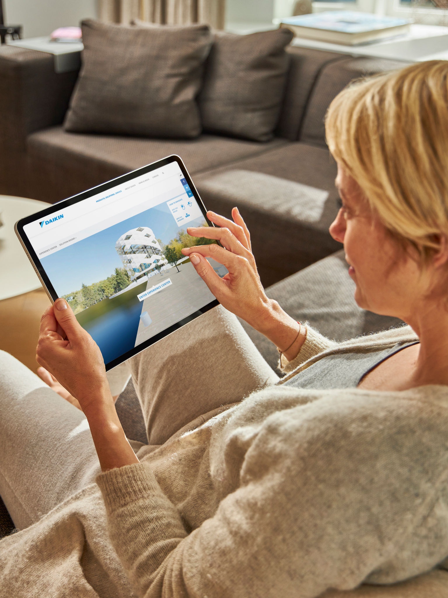 Žena sedí na pohovke a vo virtuálnom zážitkovom centre na tablete si pozerá klimatizácie