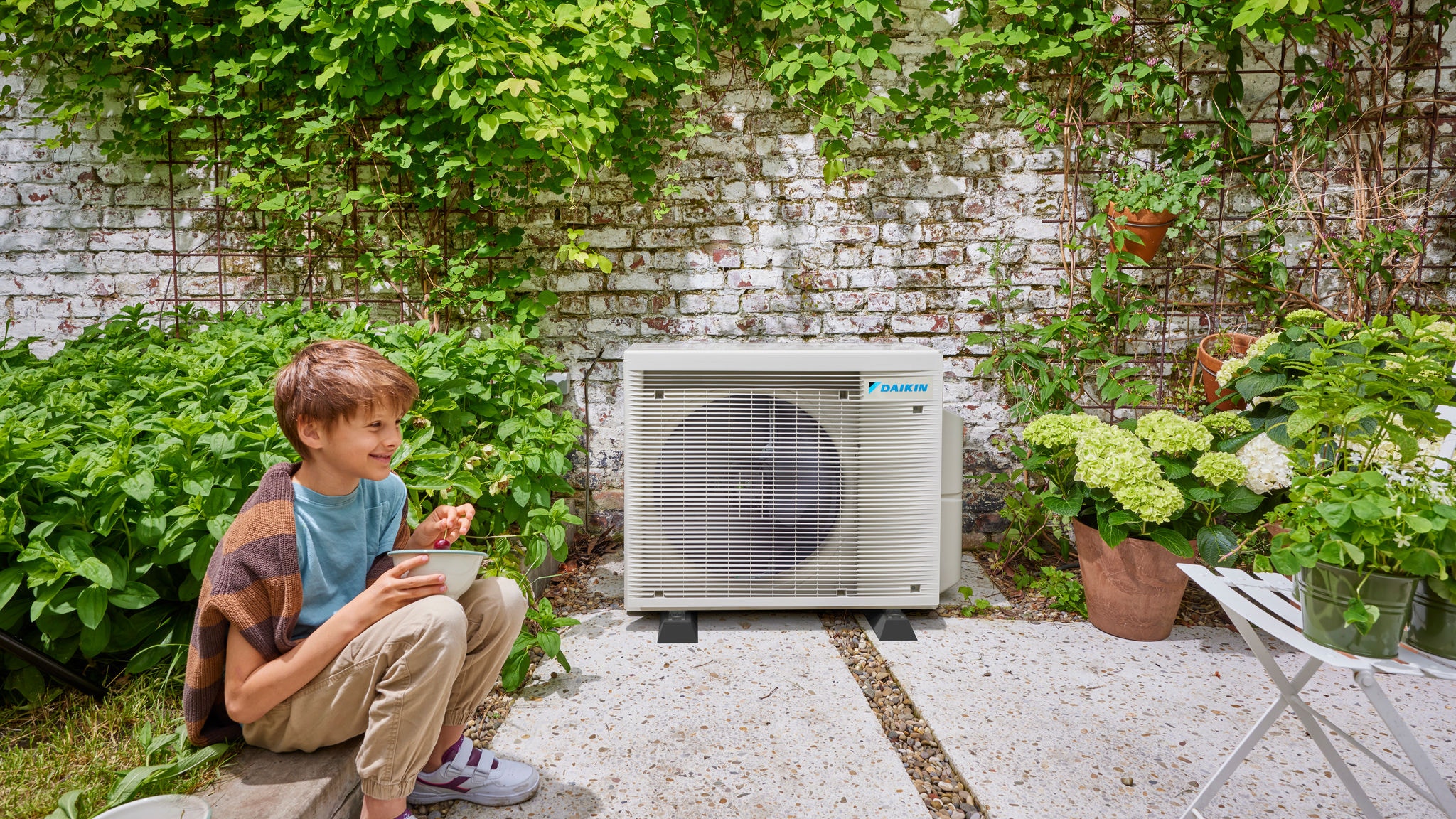 Dieťa v blízkosti vonkajšej jednotky hybridného tepelného čerpadla Daikin, ktorá kombinuje úsporu energie a pekný dizajn