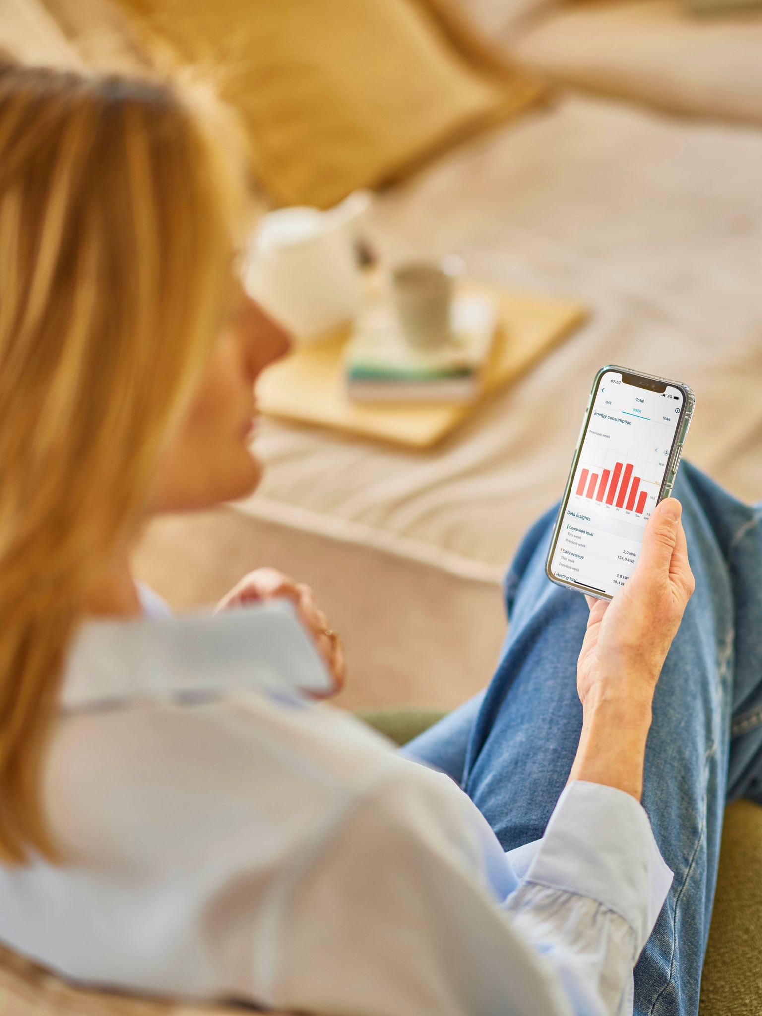 Žena s blond vlasmi si pozerá spotrebu energie v aplikácii na telefóne.