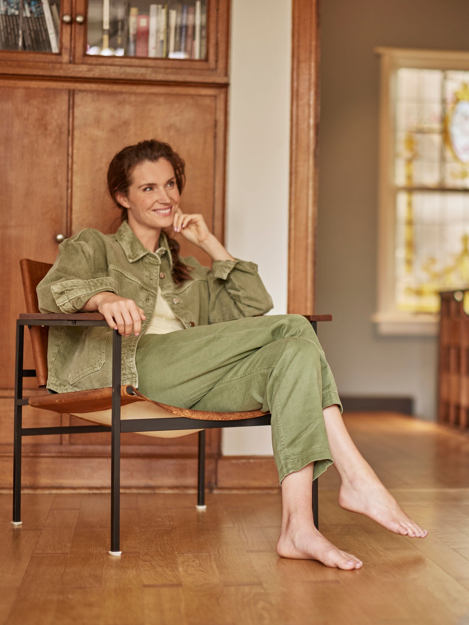 Žena sedí bosá v kresle, usmieva sa a pozerá pred seba.