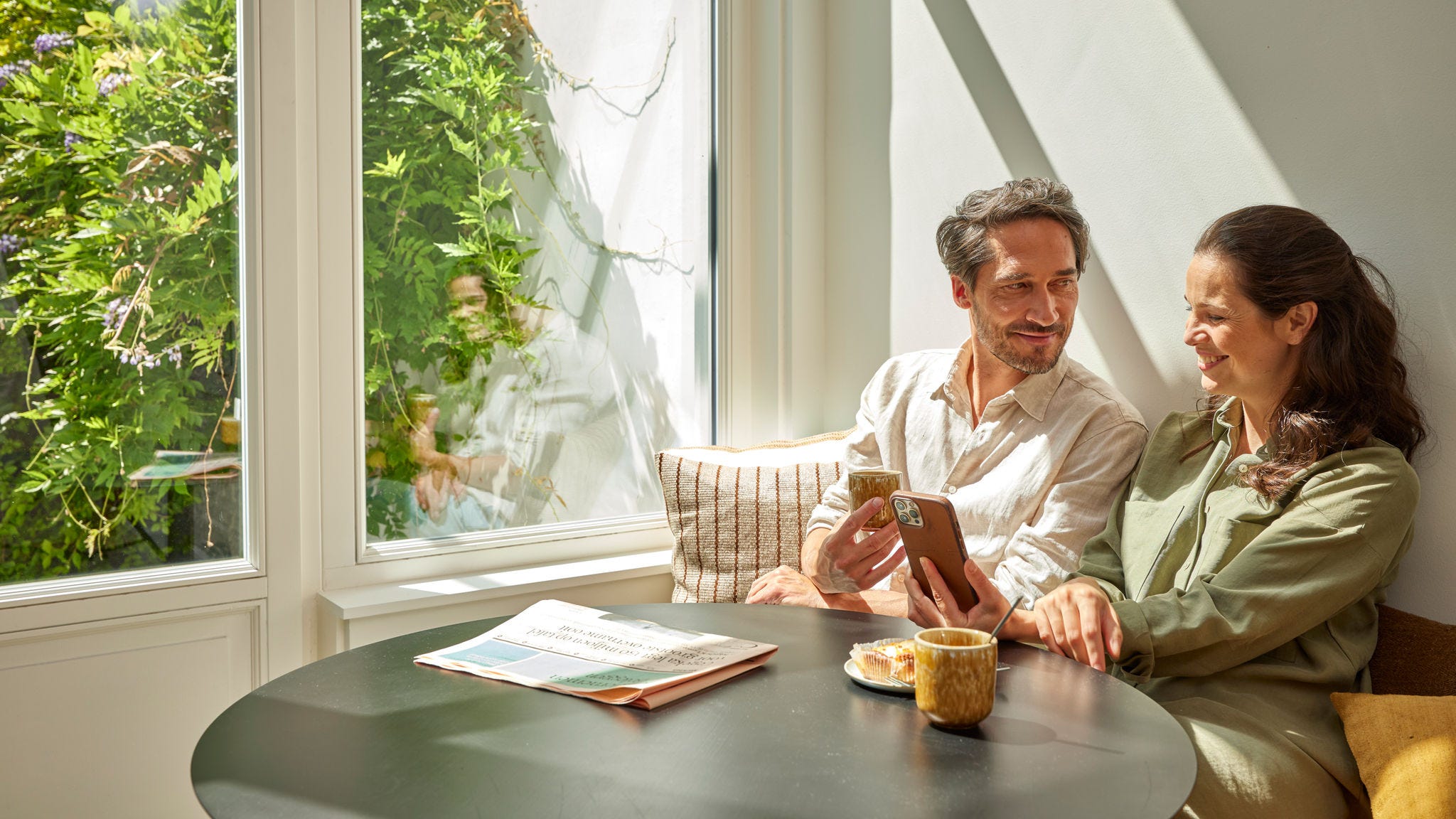 Pár si vychutnáva kávu a na telefóne kontroluje úspory energie vďaka tepelnému čerpadlu, ktoré sa premietajú do nižších nákladov