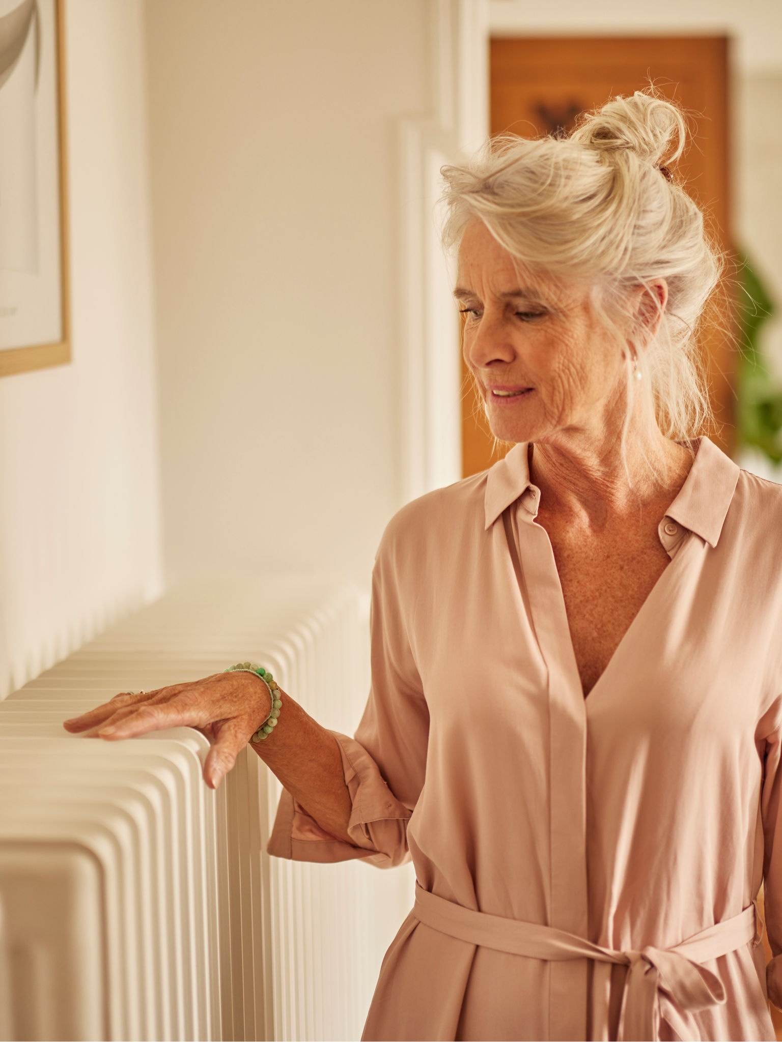 Žena si zohrieva ruky na radiátore v spálni, ktorý je spárovaný s tepelným čerpadlom využívajúcim vzduch.
