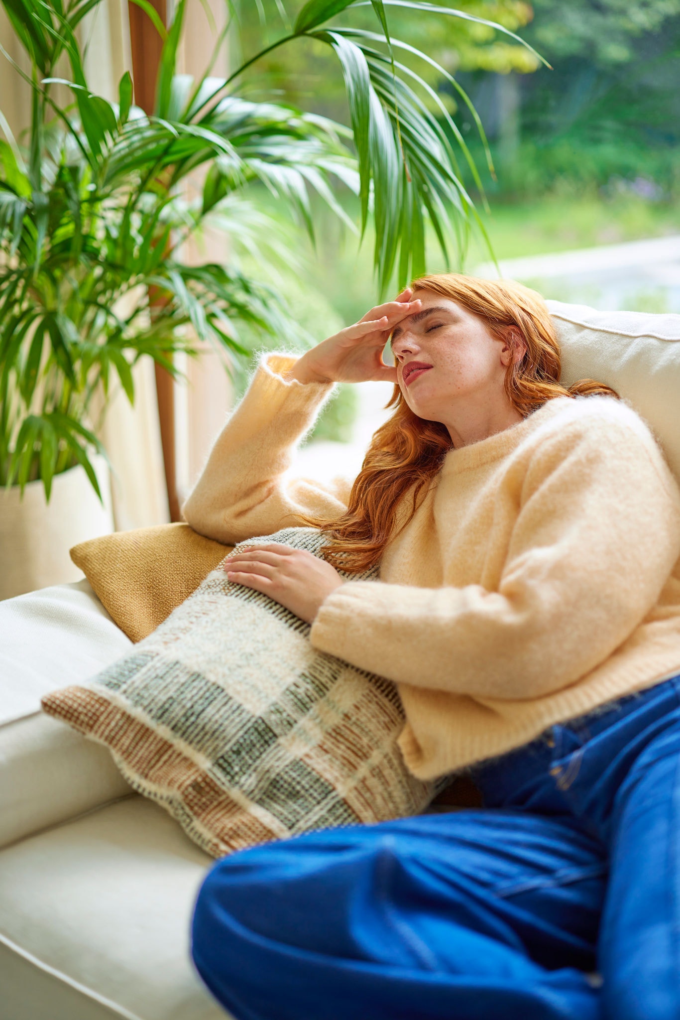 Dievča na gauči sa necíti dobre a bolí ju hlava, čo poukazuje na vplyv zlej kvality vzduchu a potrebu správneho vetrania