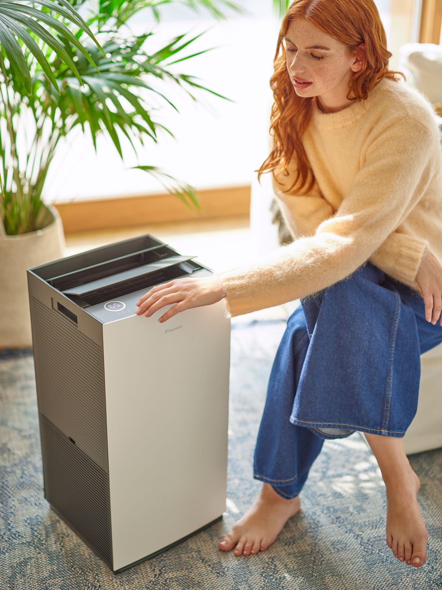 Žena v obývacom priestore nastavuje ovládače čističky vzduchu Daikin.