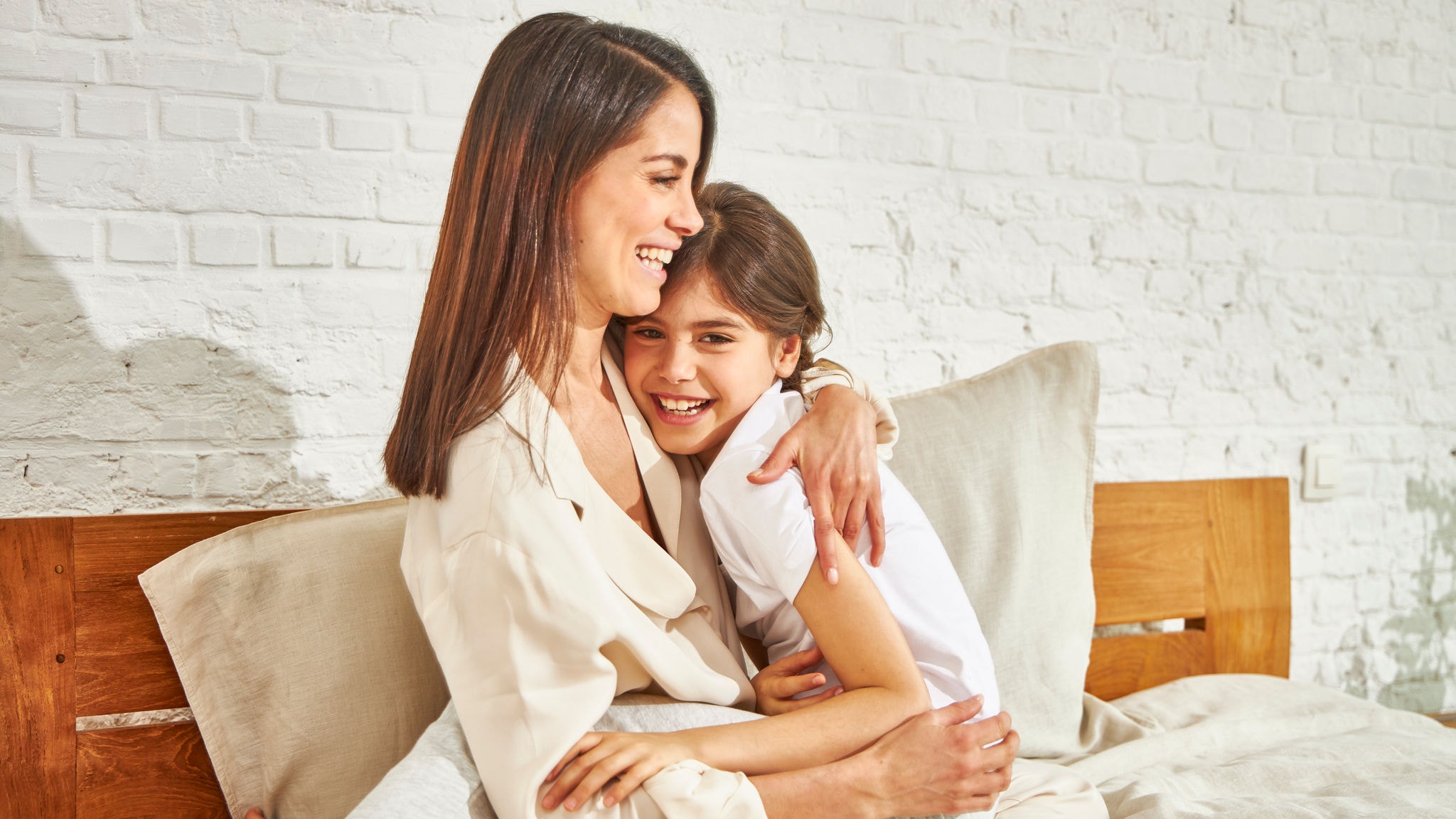 Mama s dcérou sedia na posteli a smejúc sa objímajú