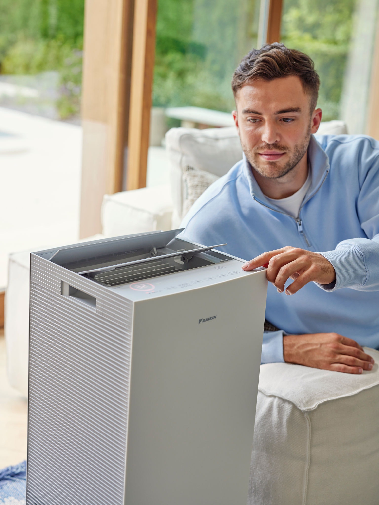 Muž nastavuje čističku vzduchu Daikin v obývacej izbe, aby znížil množstvo mačacích alergénov.