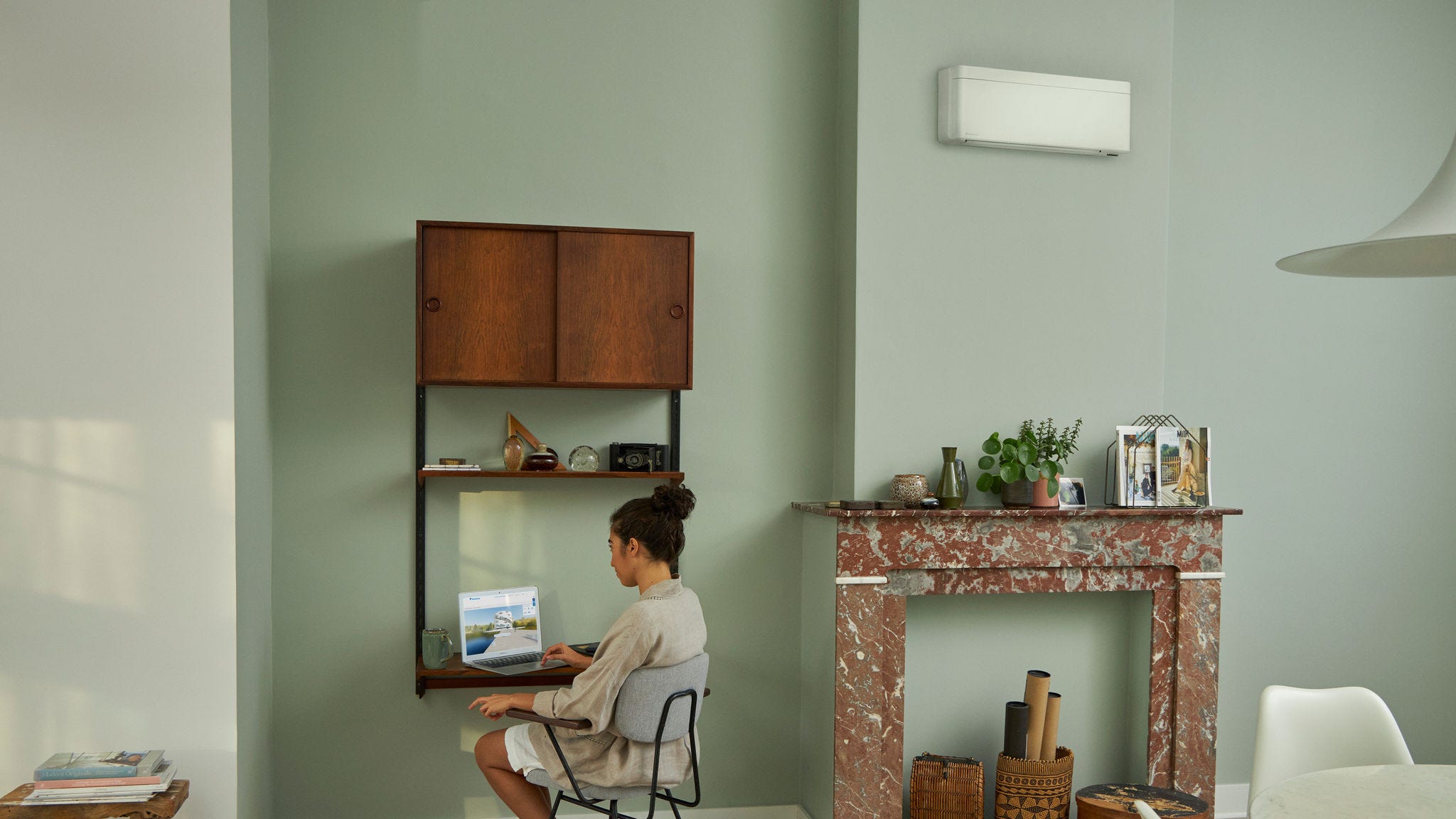 Žena si prezerá virtuálne zážitkové centrum Daikin na laptope za malým stolíkom v nádherne zariadenej obývacej izbe